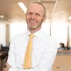 Kai Larsen in professional dress smiling with his arms crossed in an academic building.