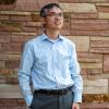 Dan Zhang in a relaxed pose near a brick wall.