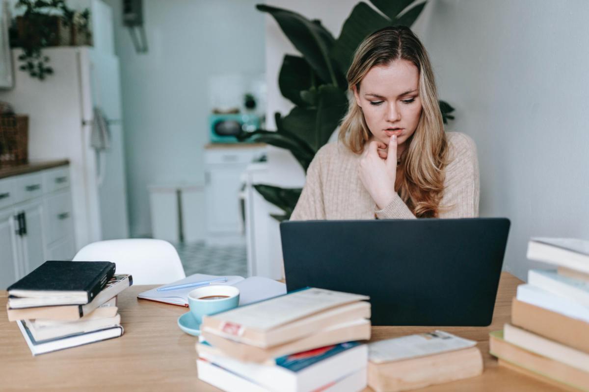 a woman at a desk with several textbooks and a laptop computer