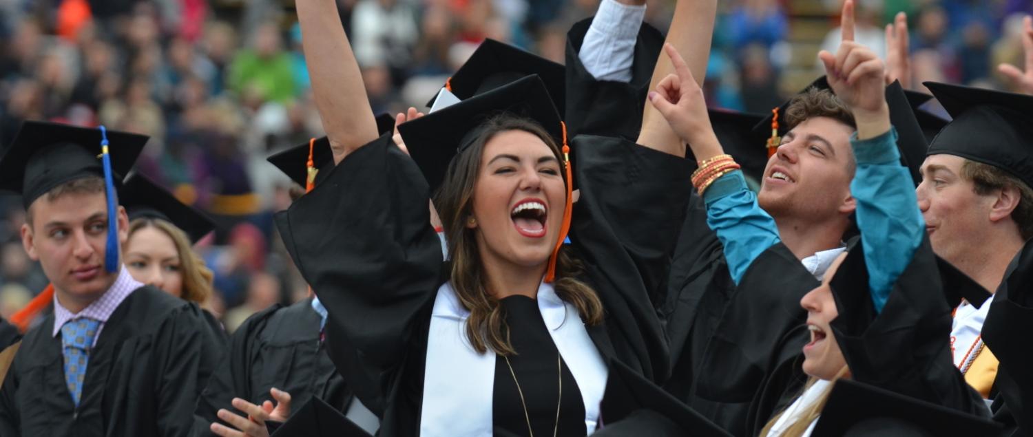 student raising hands in excitement at graduation