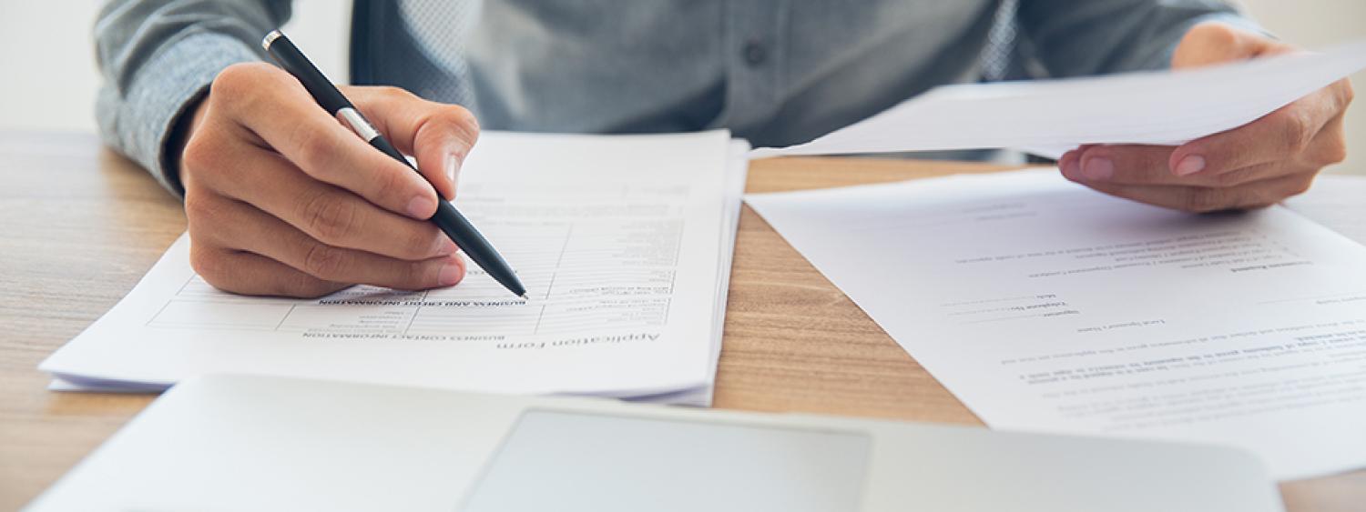 a person sitting at a desk looking through papers, holding a pen