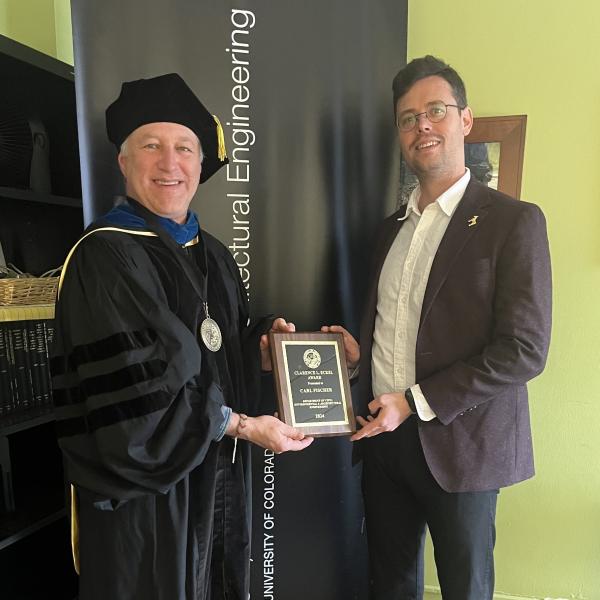 Karl Linden holds the Eckel Award plaque with Carl Fischer, the winner of the award. Karl is in graduation regalia and Carkl is in a suit.