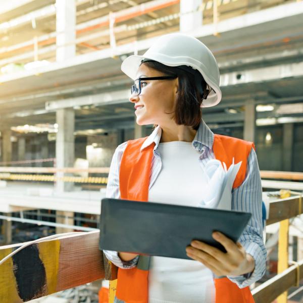 A woman in a hard hat holding a clip board inside a building that is being built.