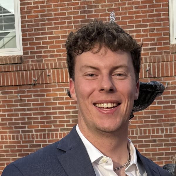 Kale Dohrman in a suitcoat and buttonp-down shirt in front of a brick wall.