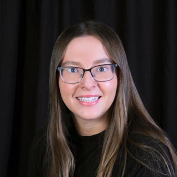 Trinity Turner wearing glasses and a short-sleeve shirt and sitting against a black background.