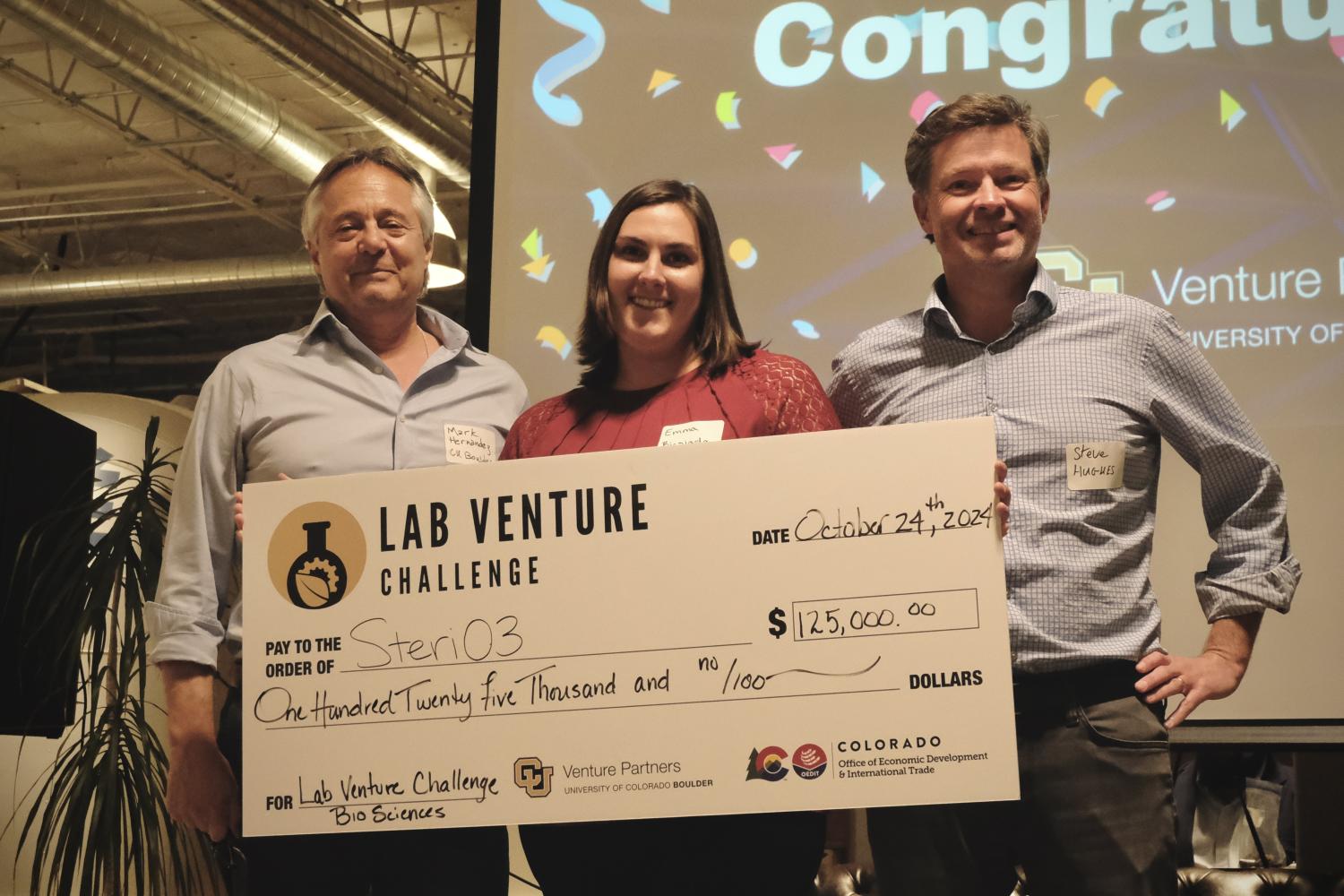 Mark Hernandez, Emmalee Biesiada and Steve Hughes hold a huge check from the Lab Venture Challenge in front of a screen that says, "Congratulations!"
