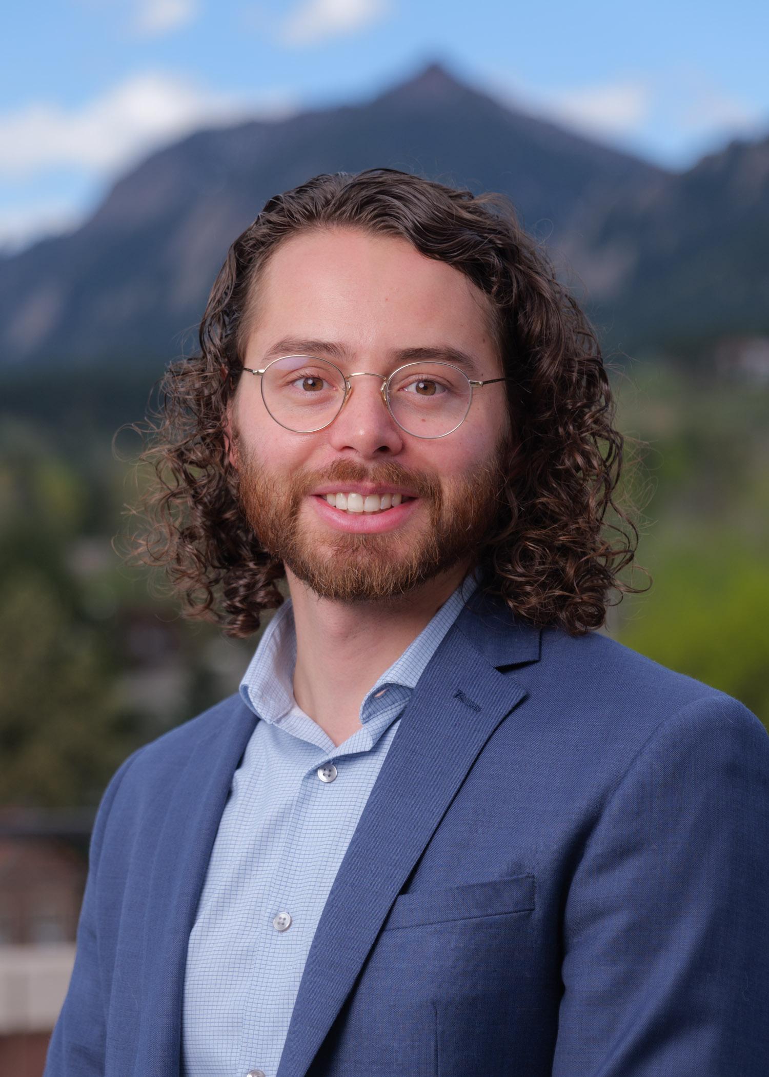 Anthony Straub in a jacket and button-down shirt with the Flatirons blurred in the background.
