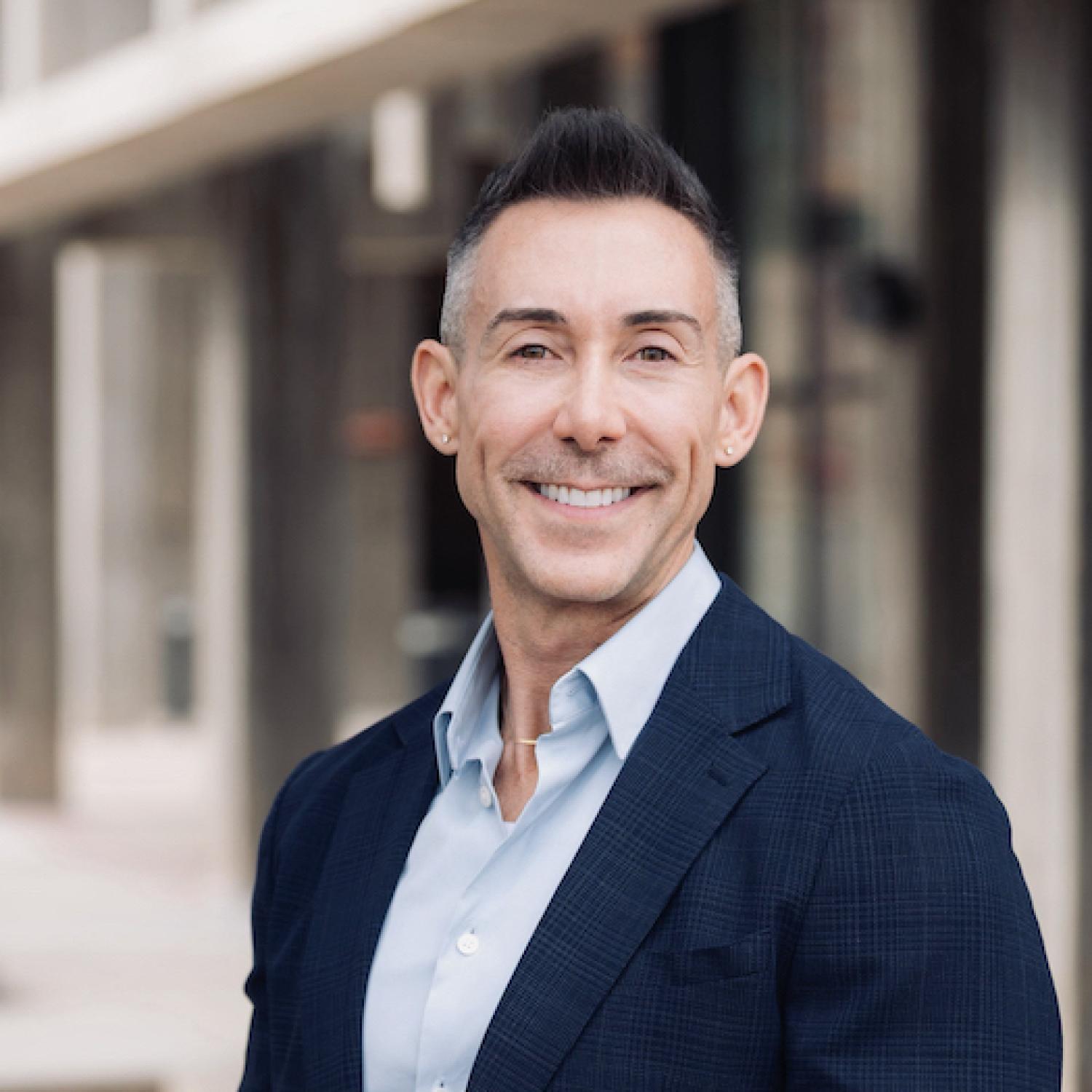 Wil Srubar in a sports coat and button-down shirt with a faded building in the background.