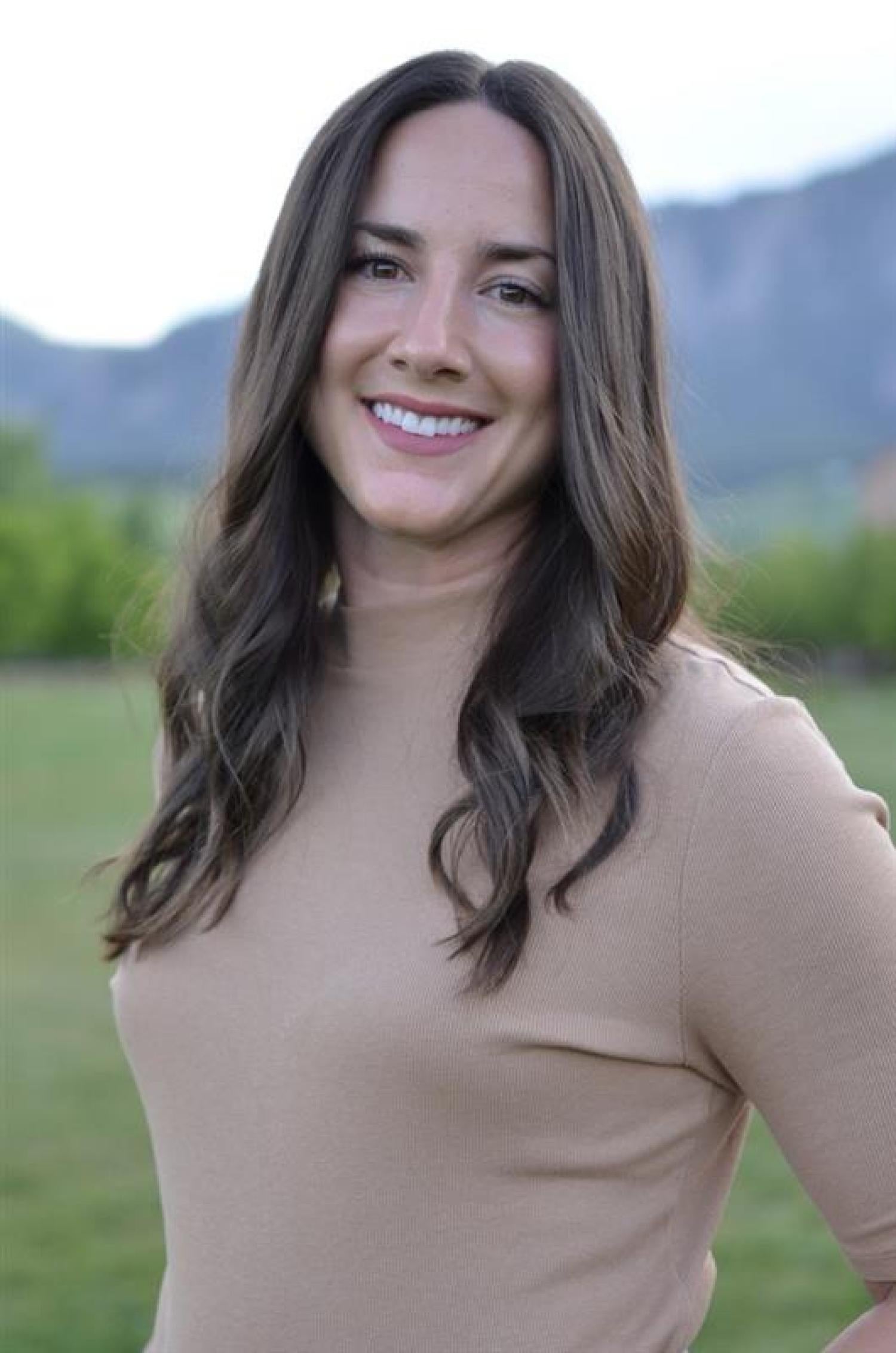 Woman from waist up smiling with mountains behind her in the distance