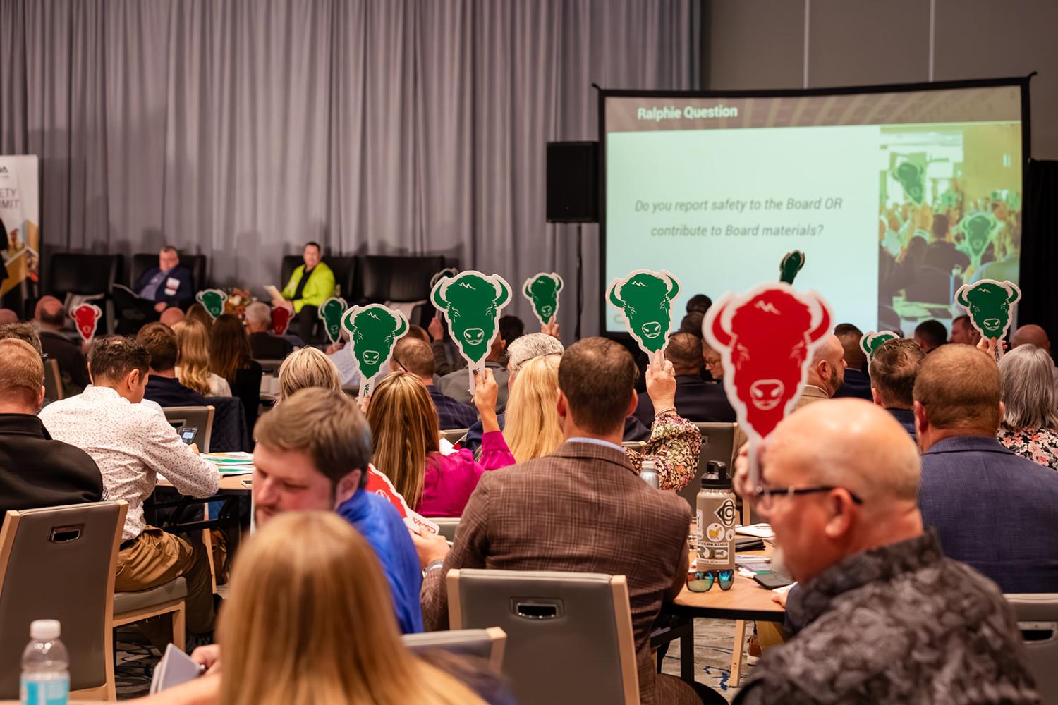 Audience members at a conference raise green and red buffalo-shaped paddles to answer a question projected on a screen during a panel session at the 2025 CSRA Safety Summit.