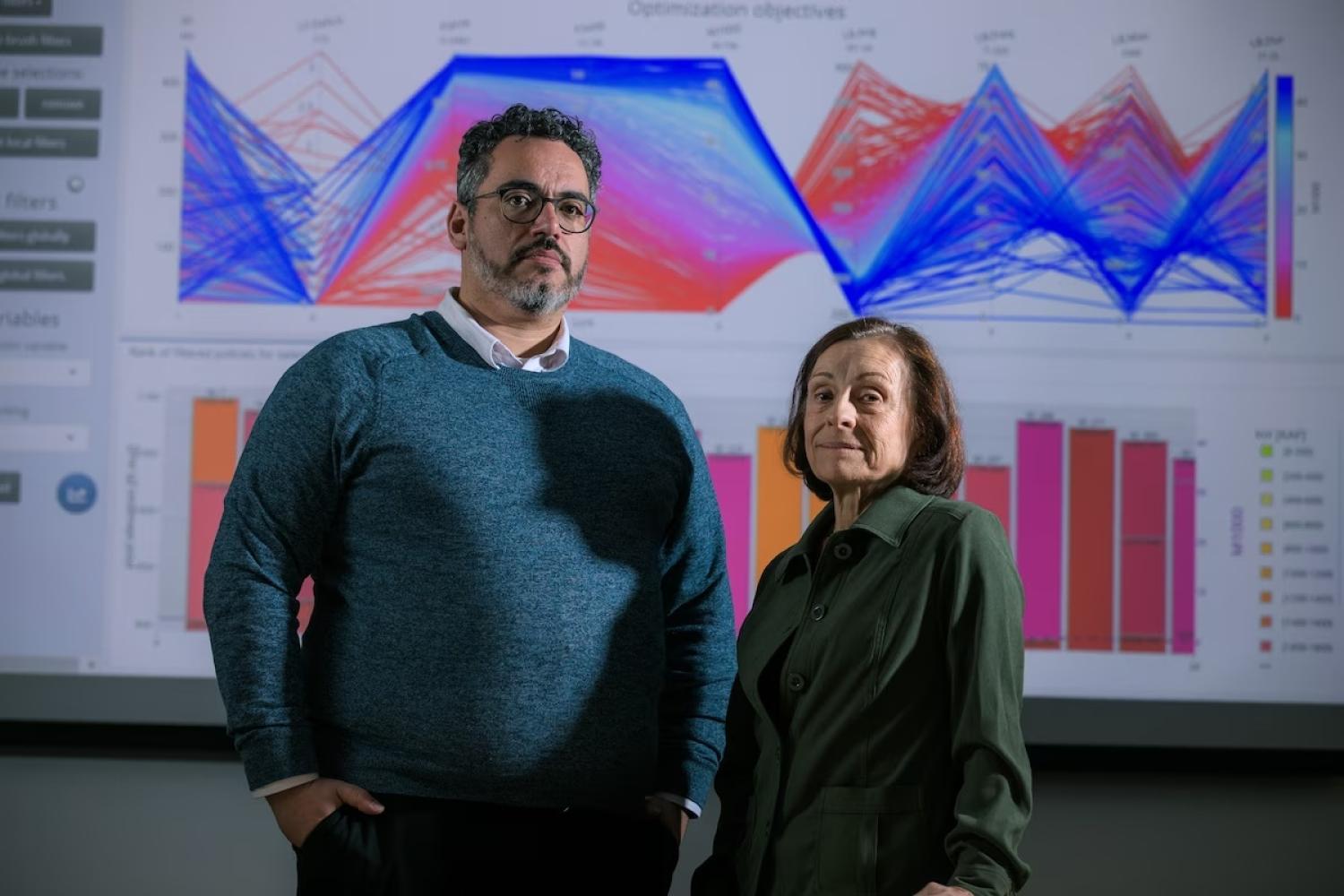 Joseph Kaspryzk and Edith Zagona in front of a wall of colorful graphics.