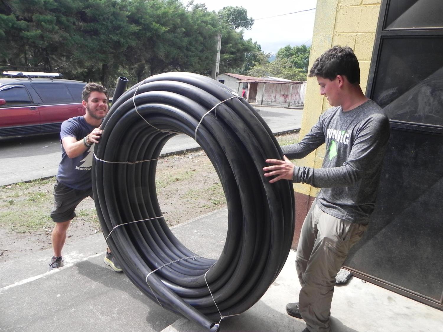 Two students rolling a 100m bundle of HDPE tubing.
