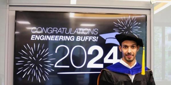 Osamah Dehwah in graduation regalia in front of a "Congratulations Engineering Buffs " digital screen.