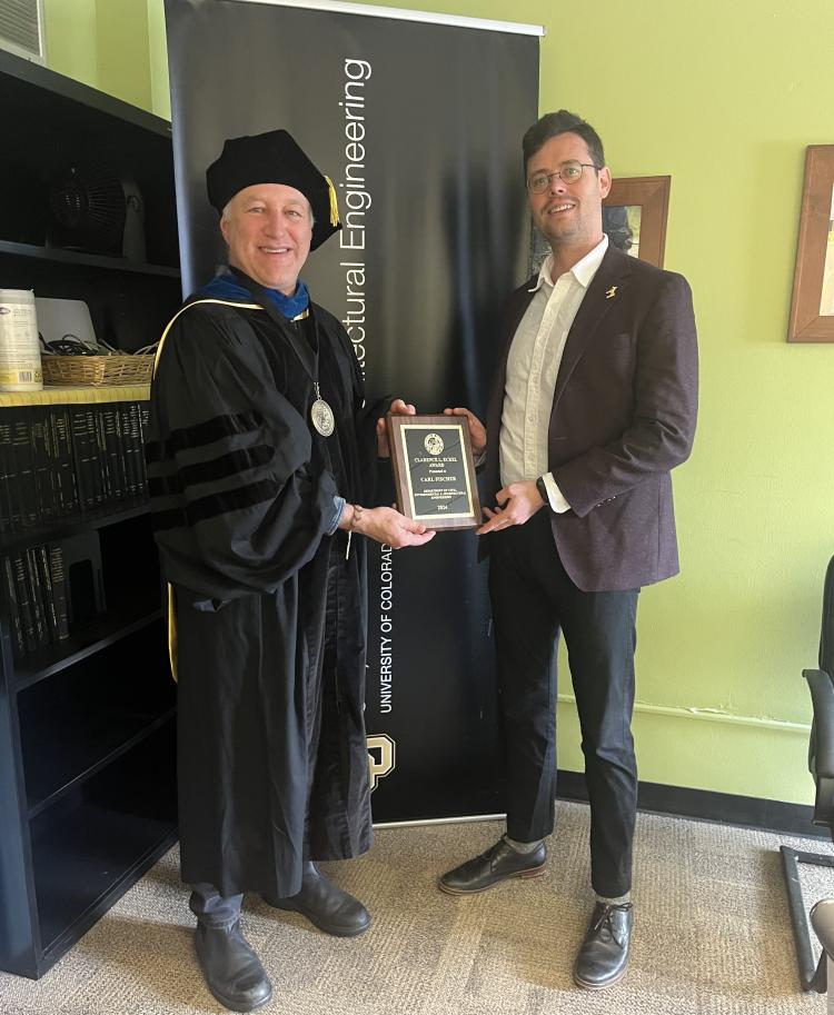 Karl Linden holds the Eckel Award plaque with Carl Fischer, the winner of the award. Karl is in graduation regalia and Carkl is in a suit.