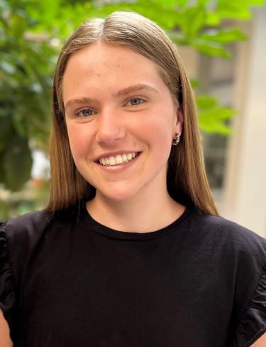 Dana Majer in a simple black top with a tree blurred in the background