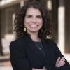 Amy Javernick-Will wearing a black blazer, earrings and a necklace in front of a blurred building