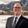 Fernando Rosario Ortiz, dressed in a suit and tie, in front of snow-covered grass, and behind that, partially snow-covered Flatirons.