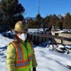 Abbie Liel in a face mask and bright clothing in front of a burned house in the snow from the Marshall fire