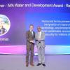 Evan Thomas and another man stand on a stage holding an award during a formal ceremony. A large screen behind them reads &ldquo;Winner &ndash; IWA Water and Development Award &ndash; Research&rdquo; and displays the name Evan Thomas, along with text honoring his contributions to sustainable water security.