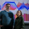 Joseph Kaspryzk and Edith Zagona in front of a wall of colorful graphics.