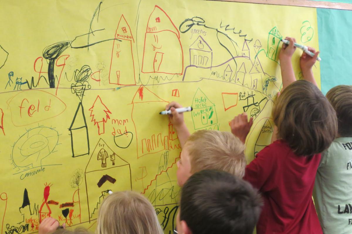 Children drawing with markers their vision of a town on paper pinned to the wall.