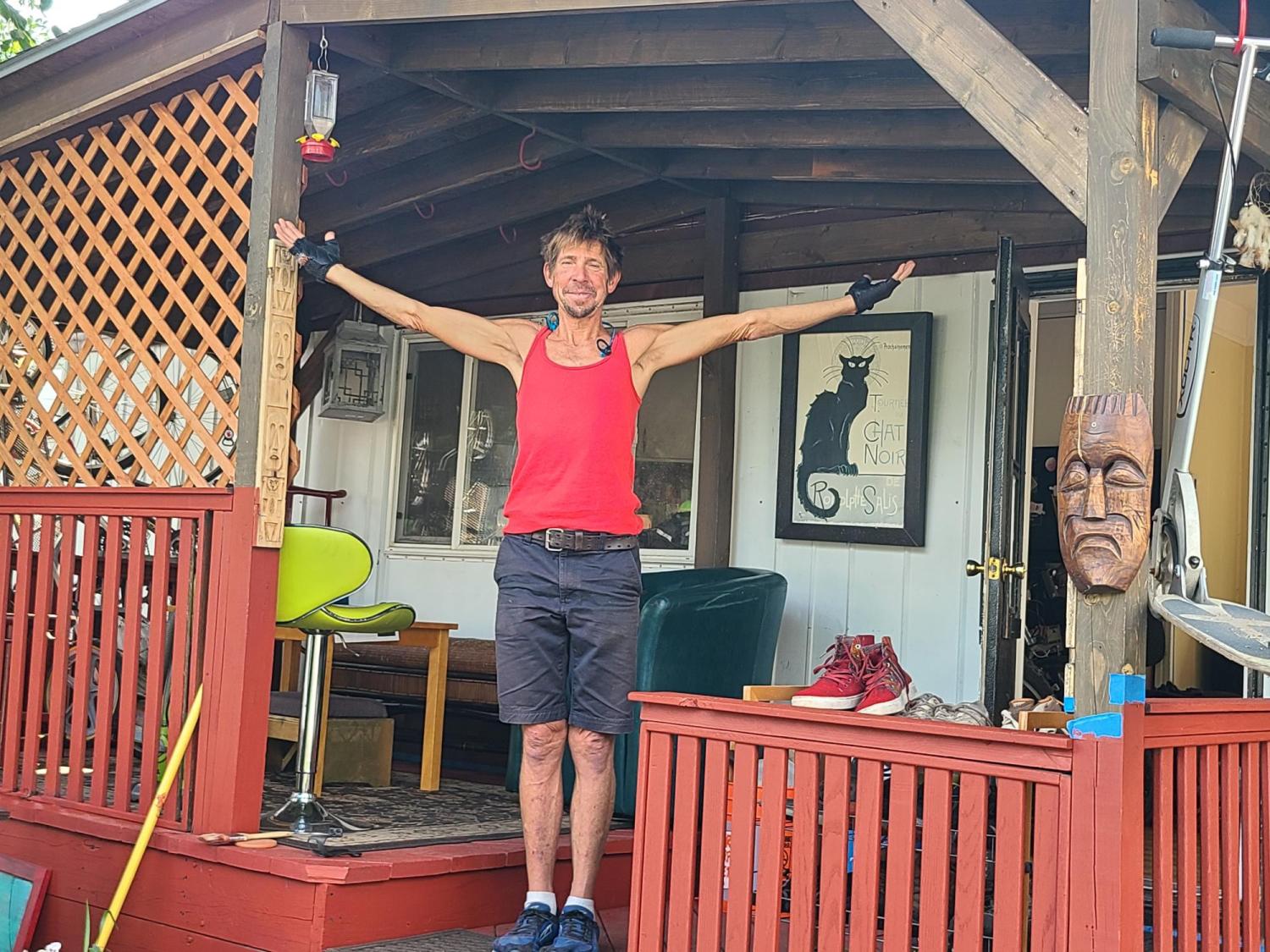 Dave Weil with his arms spread out on the porch of his mobile home.