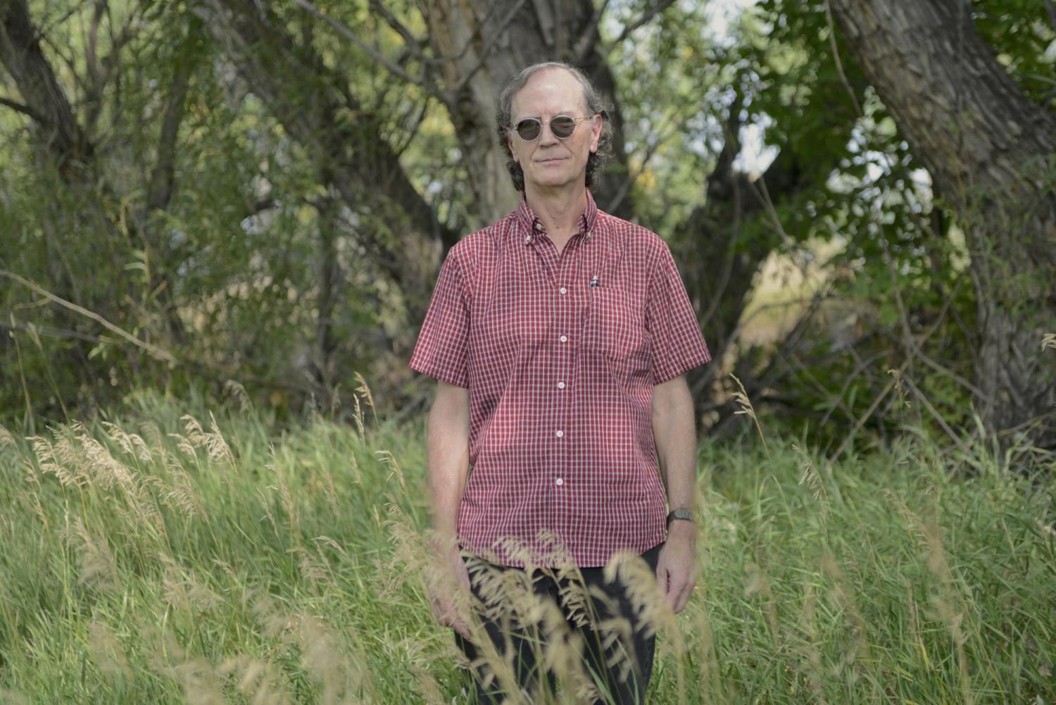 Michael Peirce stands in tall grass in front of blurred out trees.