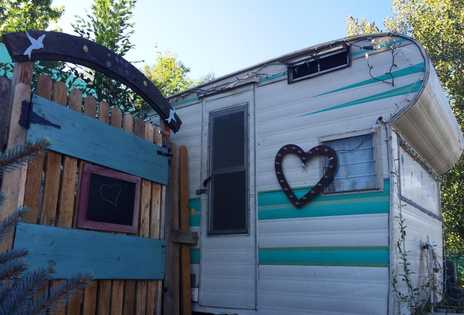 An older RV with a heart on it next to a wooden fence.