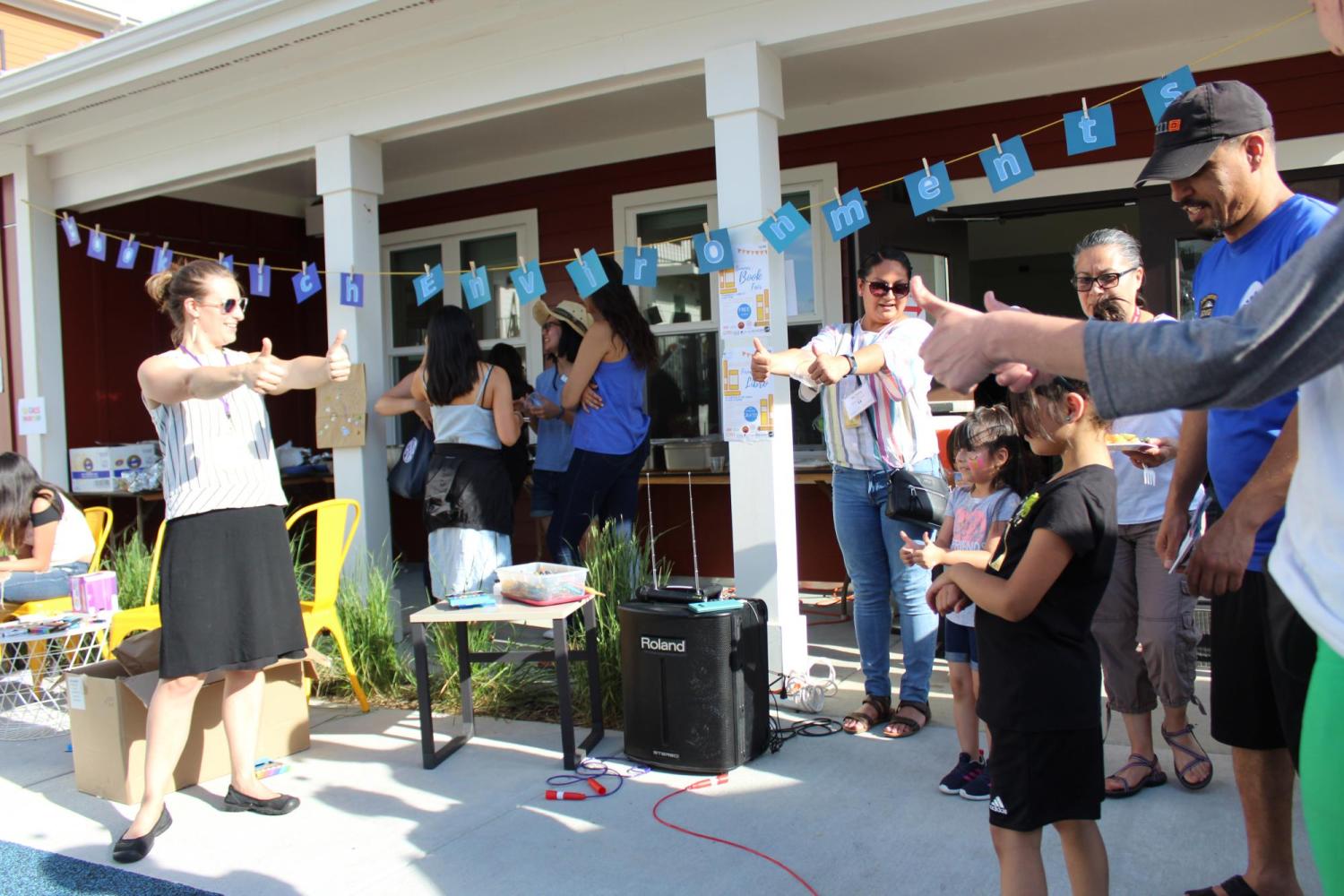 Children and adults stand in a circle giving a thumbs up at a Book Rich Environment event which brought the Moving to Work and Bringing School Home programs together.