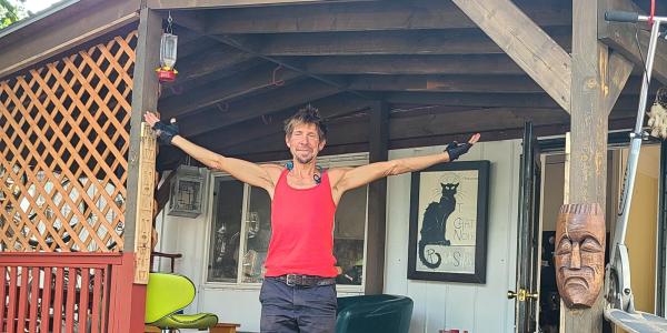 Dave Weil with arms outstretched on his porch of his manufactured home