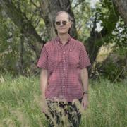 Michael Peirce stands in tall grass in front of blurred out trees.