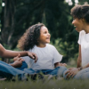 Parents sit with their child in front of a tree.