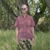 Michael Peirce stands in tall grass in front of blurred out trees.