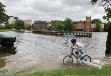 Young boy riding on his bicycle in a flooded street.