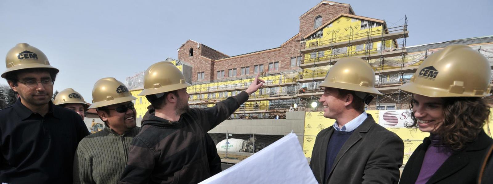 CEM faculty and students look over blueprints at a construction site.