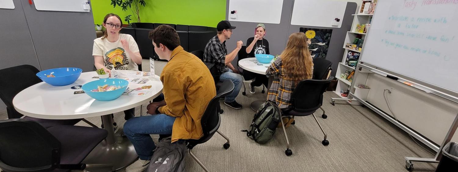 Students and tutors gather around tables with international snacks to translate recipes