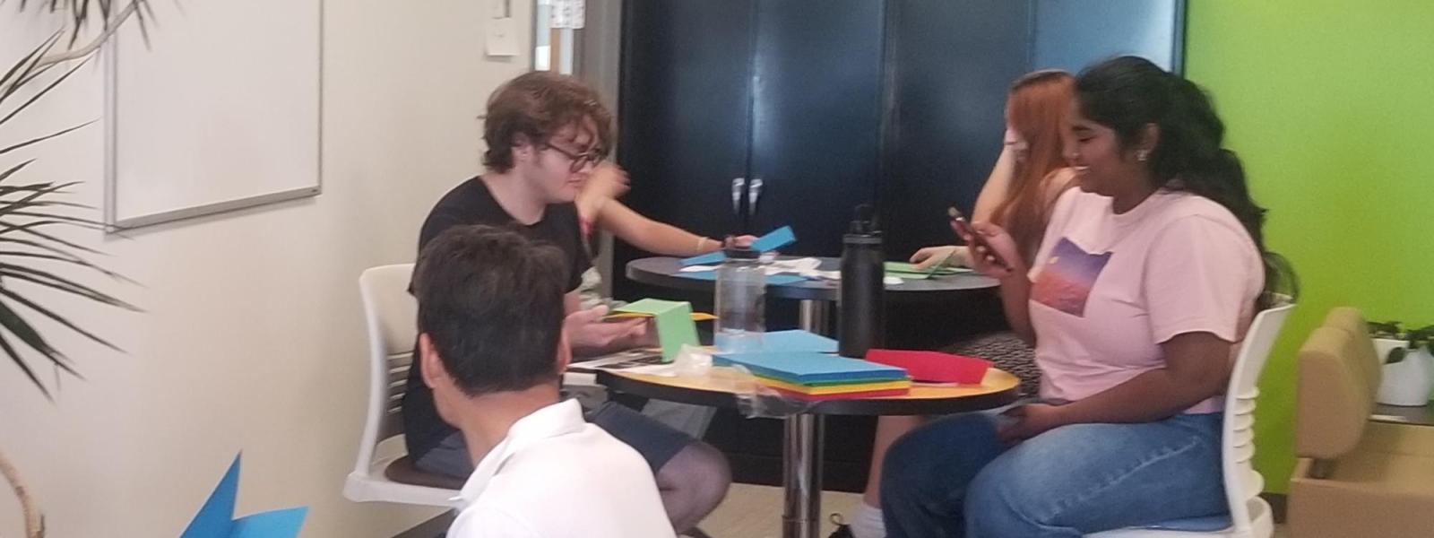 Students sitting around tables folding paper game pieces