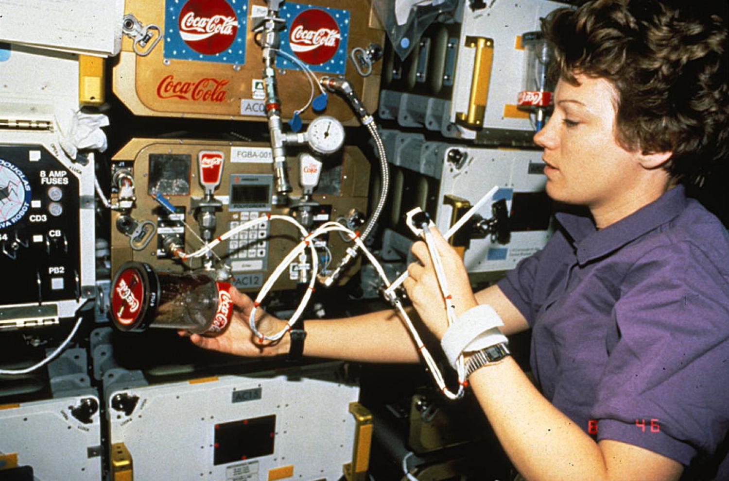 NASA astronaut Eileen Collins measuring her heart rate with FGBA-2 while holding an FTU filled with Coke