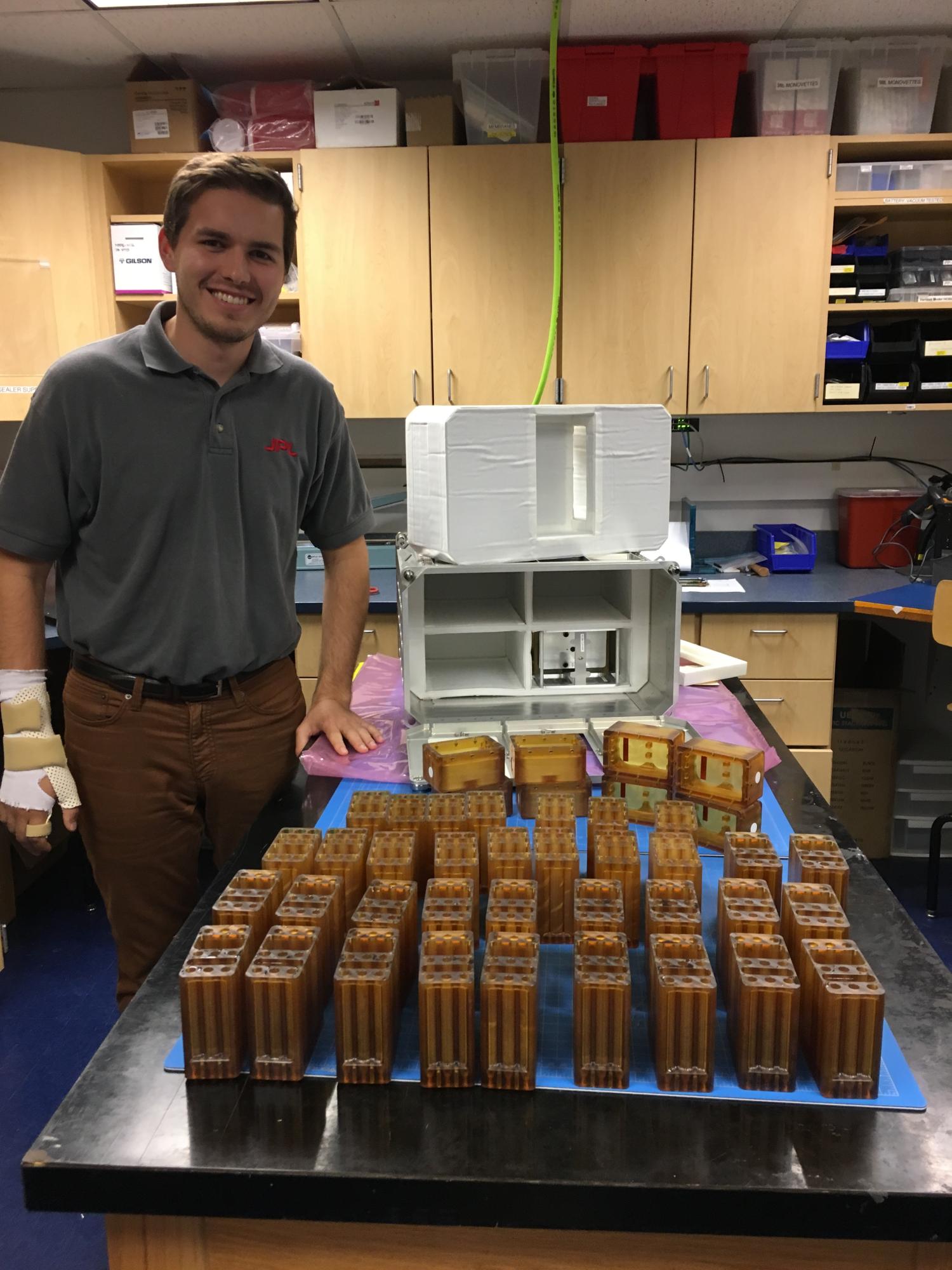 BioServe Graduate Research Assistant Arthur Barriault Standing Beside an Array of Chip Casettes and Media Casettes for use with SPOC