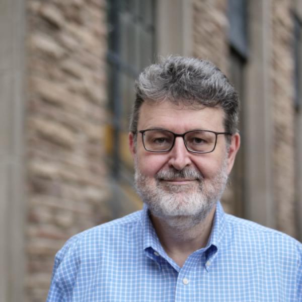 Man wearing button up shirt and glasses in front of brick building