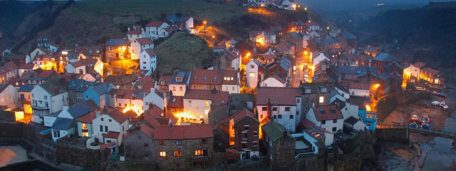 Houses all lit up in a small English village at night.