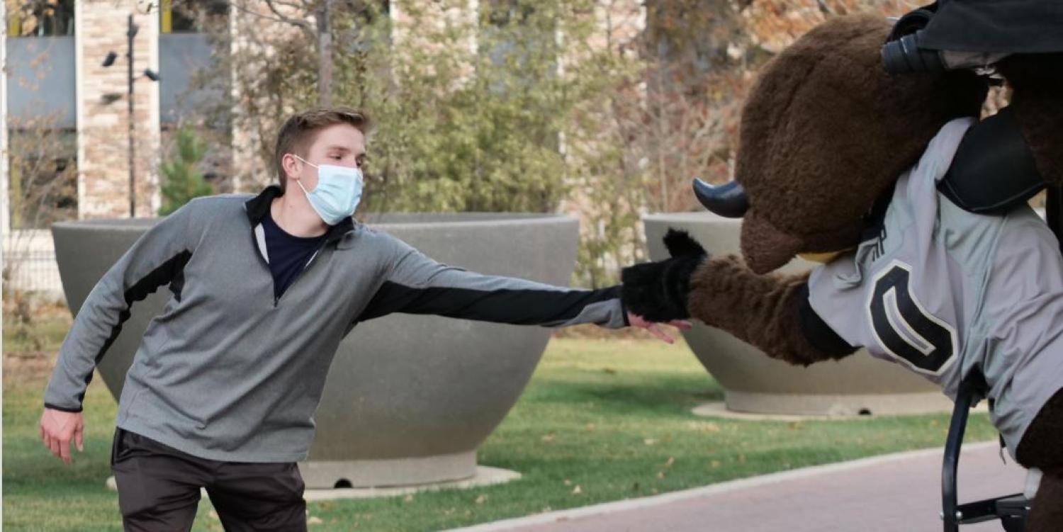 Student in mask fist bumping Ralphy the mascot