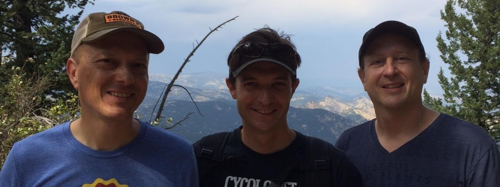 3 men facing front smiling, outside, hiking, blue sky