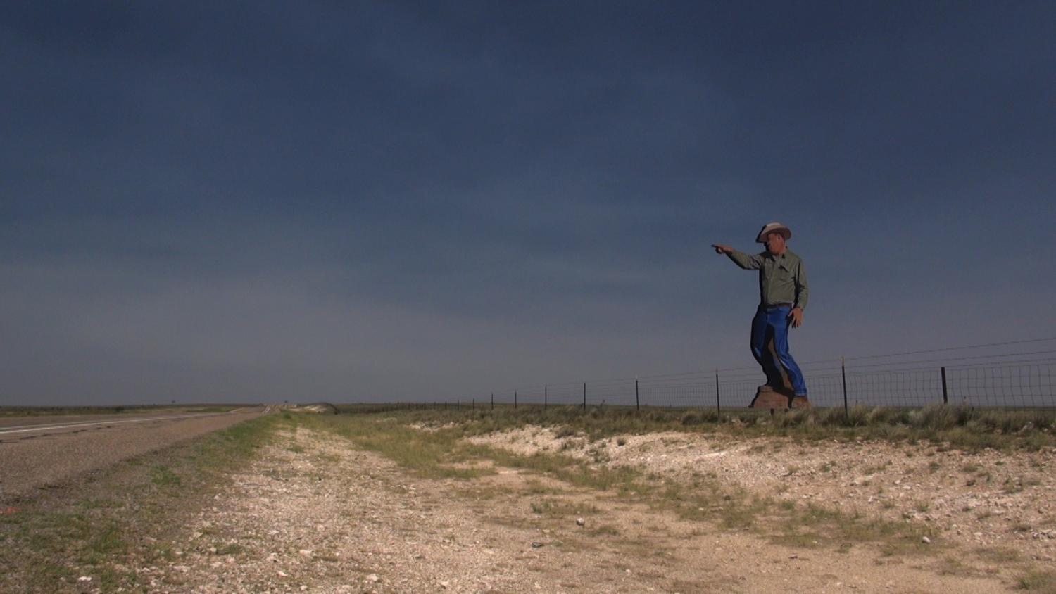 A man in a cowboy hat points at the sky over an open field.
