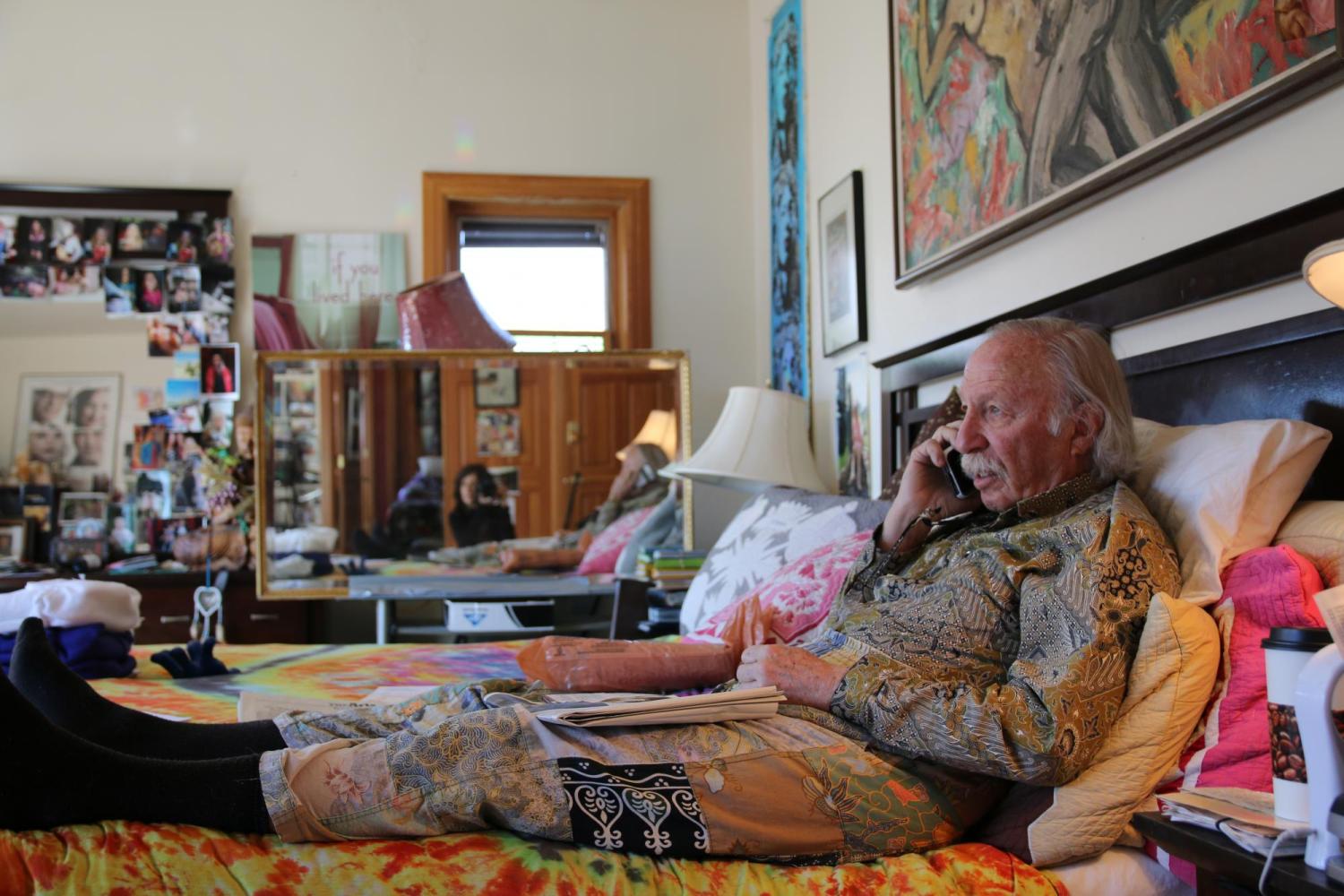 Man on bed with filmmaker Lynne Sachs visible in a mirror in the background. Still from Sachs's doucmentary Film About a Father Who (2020).