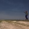 A man in a cowboy hat points at the sky over an open field.