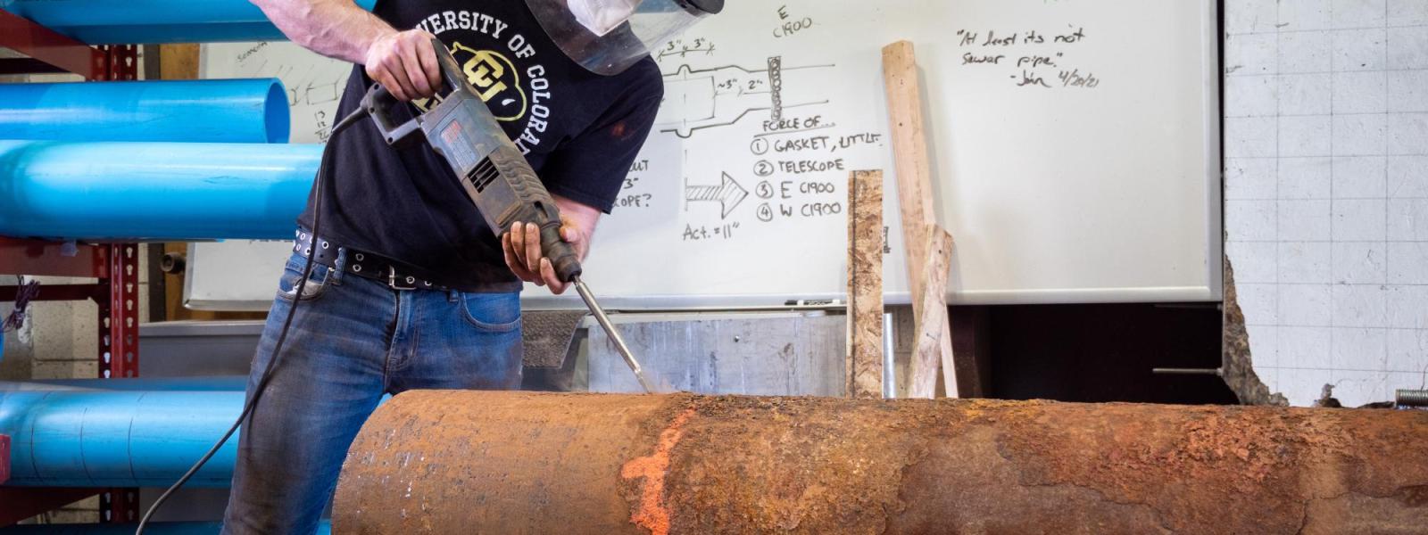 CIEST student employee using a power tool to descale a cast iron pipe removed from service for the REPAIR project