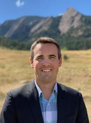 Mortenson Center Director Evan Thomas standing outside in front of a mountain backdrop