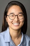 Asian woman smiling with long black hair, blue shirt and glasses