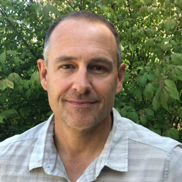Man in grey shirt stands in front of tree